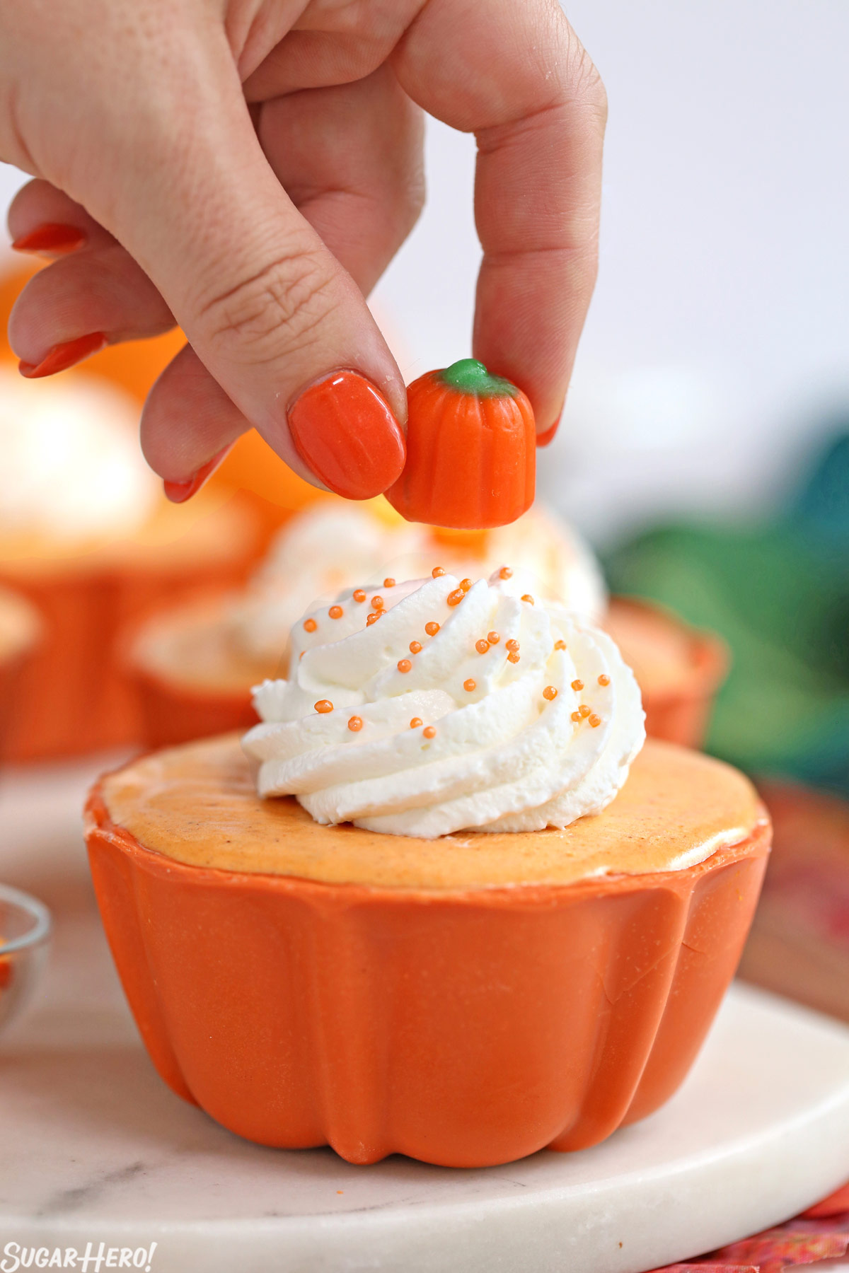 Pumpkin Spice Mousse Cups - process shot of piping whipped cream and adding candy pumpkin on top of mousse cup | From SugarHero.com