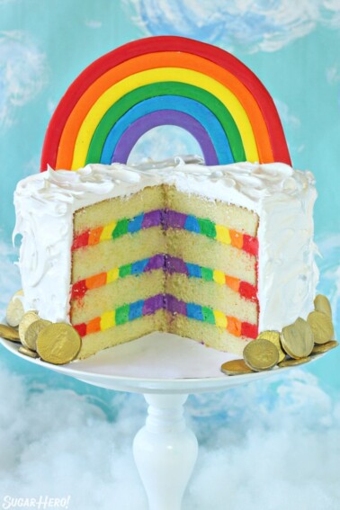 Rainbow cake with a rainbow cake topper, cut open to reveal stripes of rainbow buttercream inside.