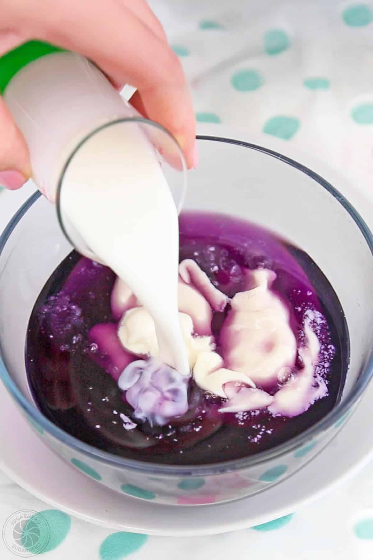 A mixing bowl of purple gelatin with yogurt and cream being added.