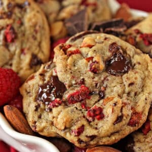 Close up of Raspberry Almond Chocolate Chunk Cookies in a white dish with raspberries and almonds scattered around.