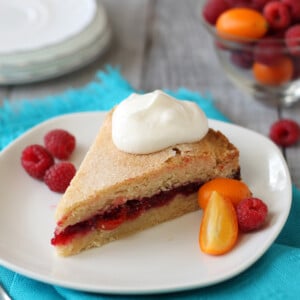 Slice of Raspberry Kumquat Sugar Cookie Cake on a white plate surrounded by fruit.