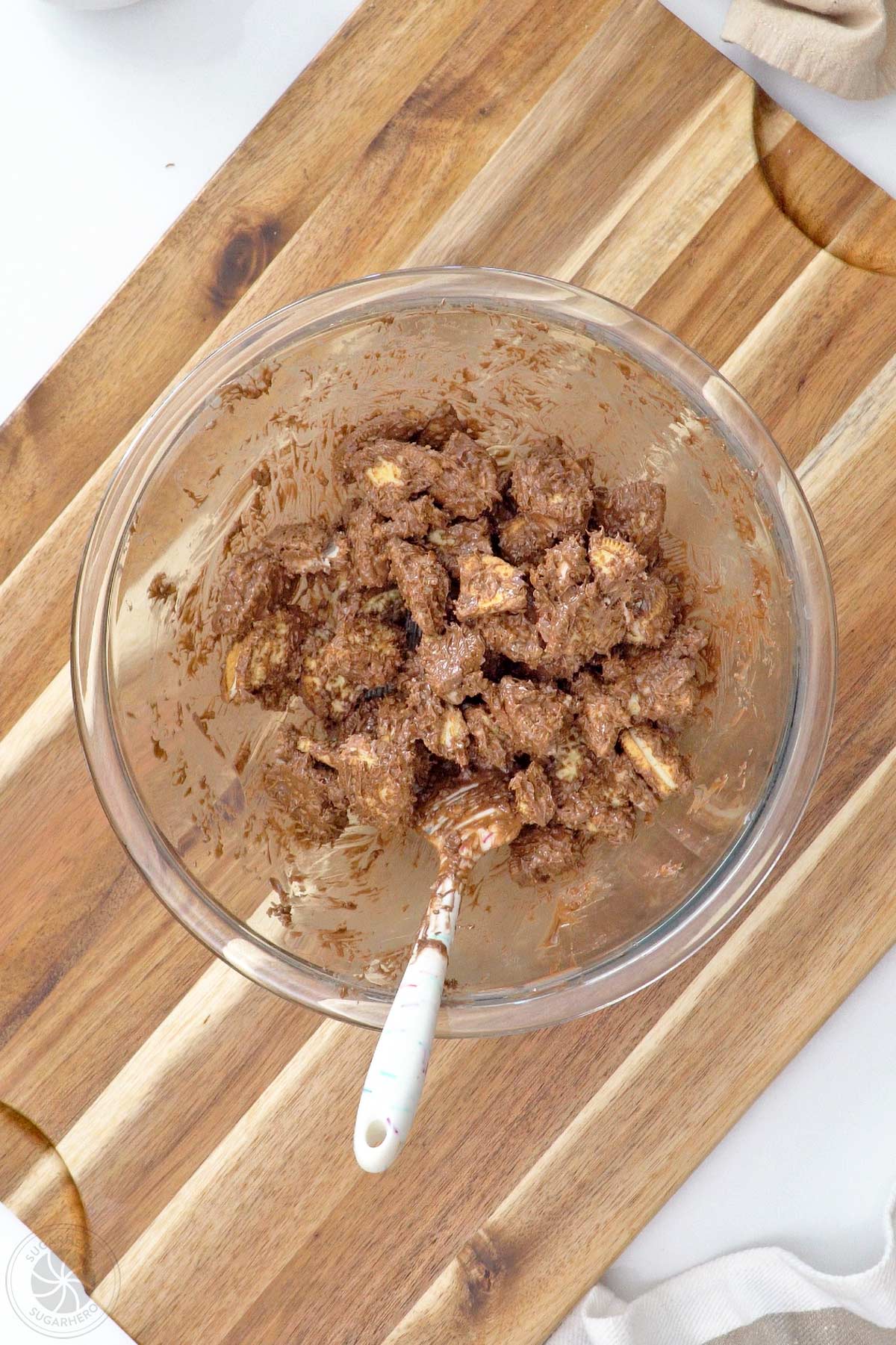 Mixture of melted coating, popping candy, and chopped cookie pieces in a large glass bowl.
