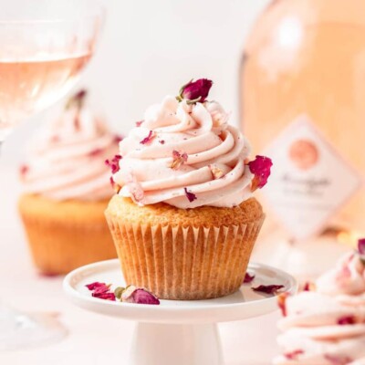 Ros&eacute; Cupcake on a small white cupcake stand, with a bottle and glass of Ros&eacute; in the background.