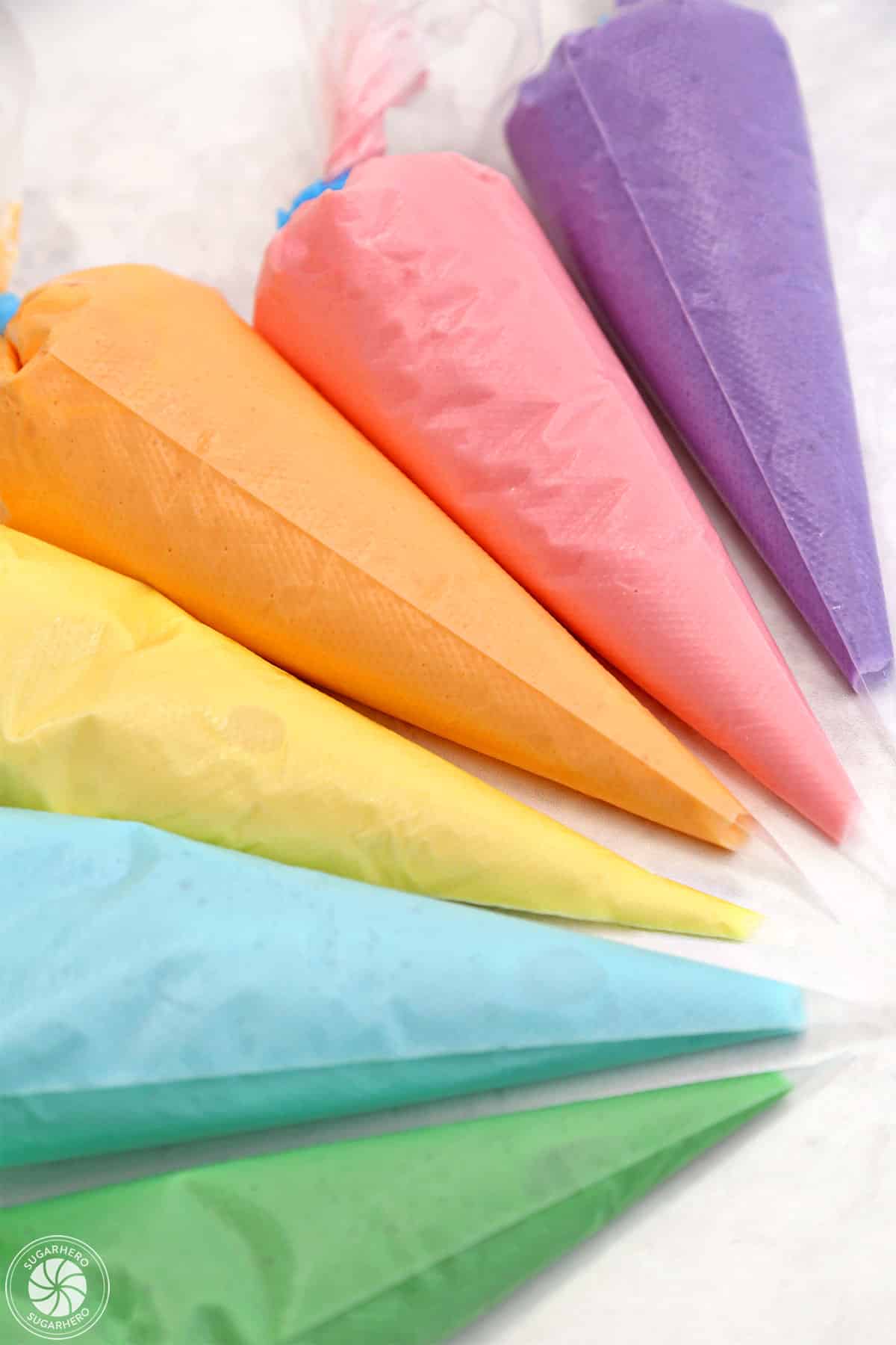 Clear piping bags holding colorful royal icing, arranged in a semi-circle.