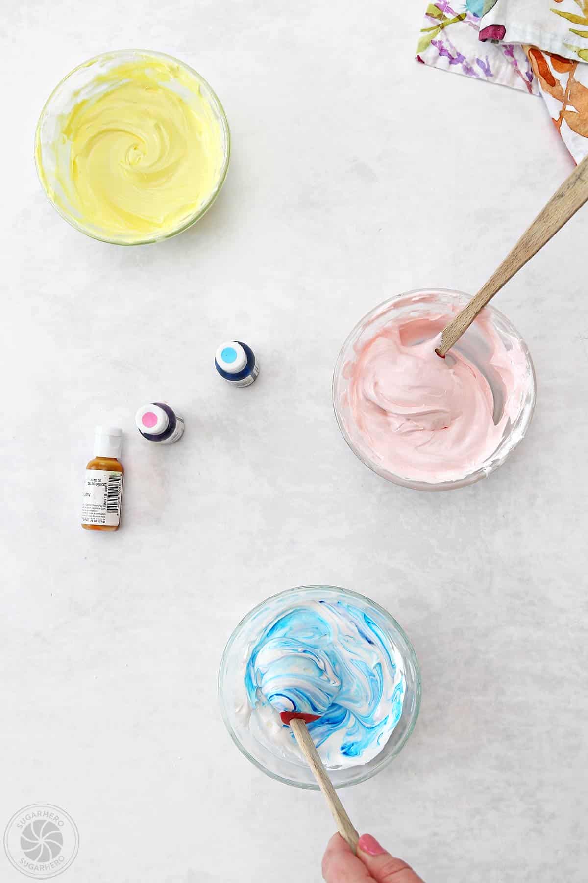 Three bowls of royal icing being colored with small bottles of gel food coloring.