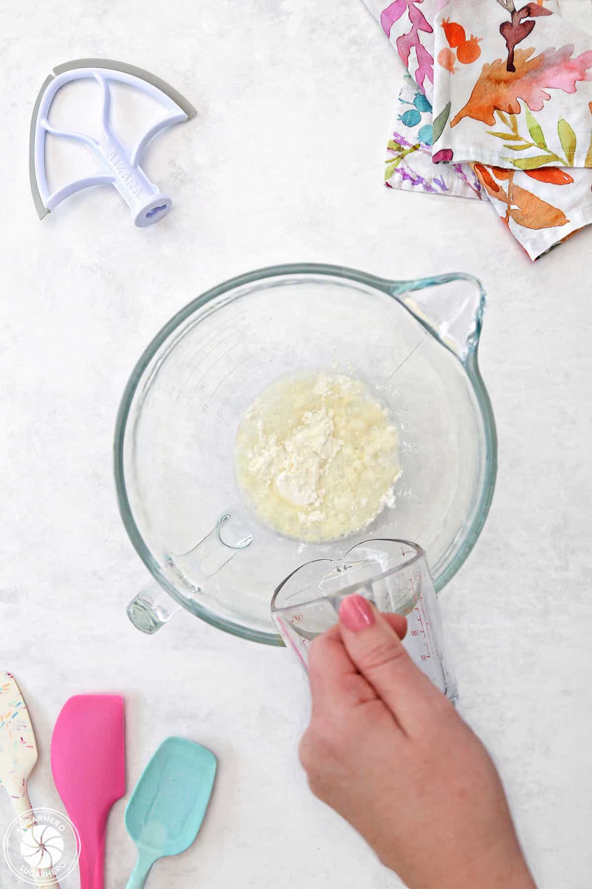 Adding water to meringue powder in a clear mixing bowl.