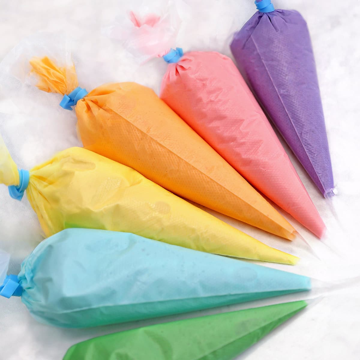 Clear piping bags holding colorful royal icing, arranged in a semi-circle.