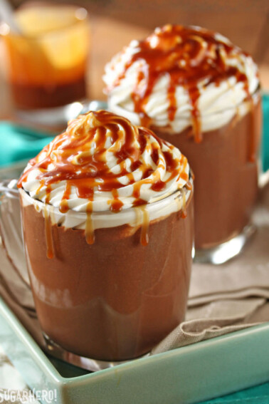 2 mugs of Salted Caramel Hot Chocolate drizzled with caramel sauce.