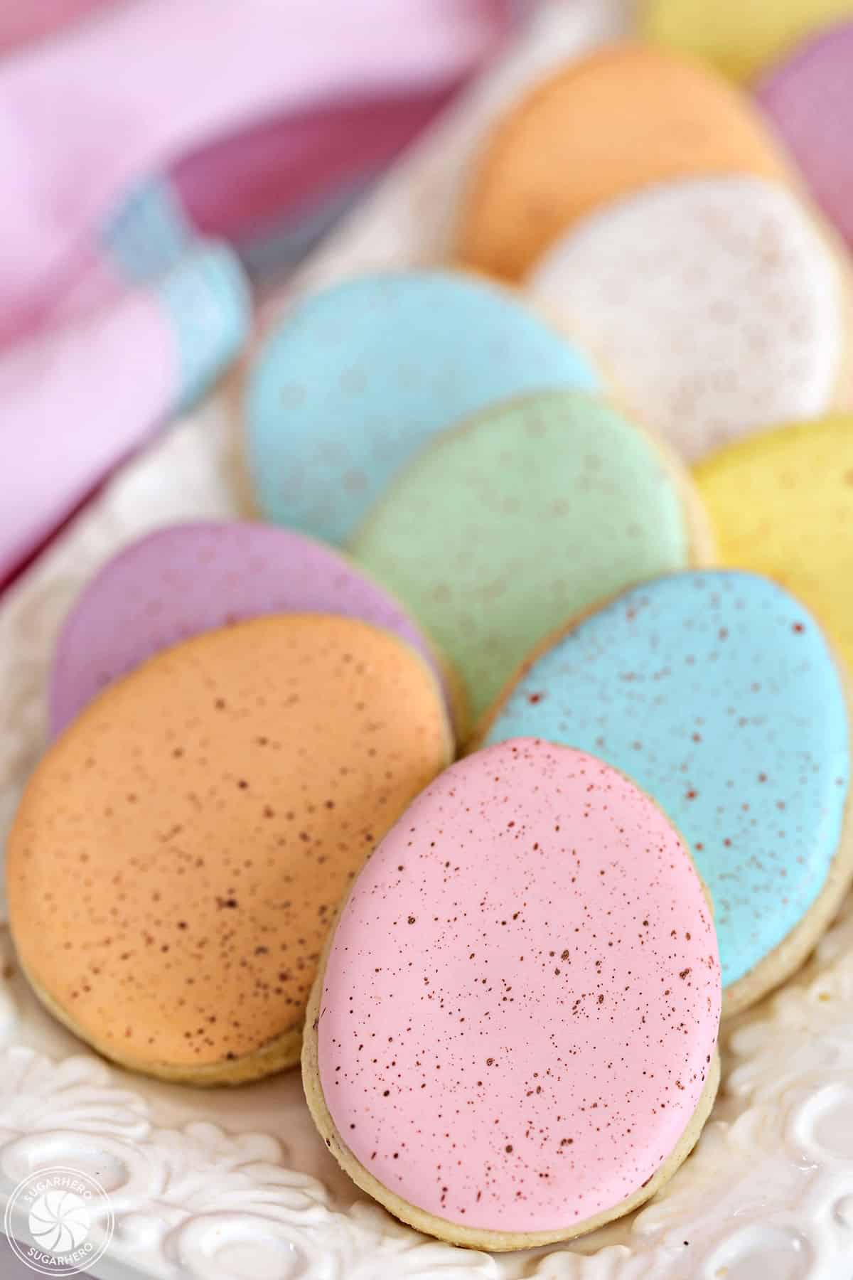 Pastel easter egg cookies on a white tray with a pink linen in the background.