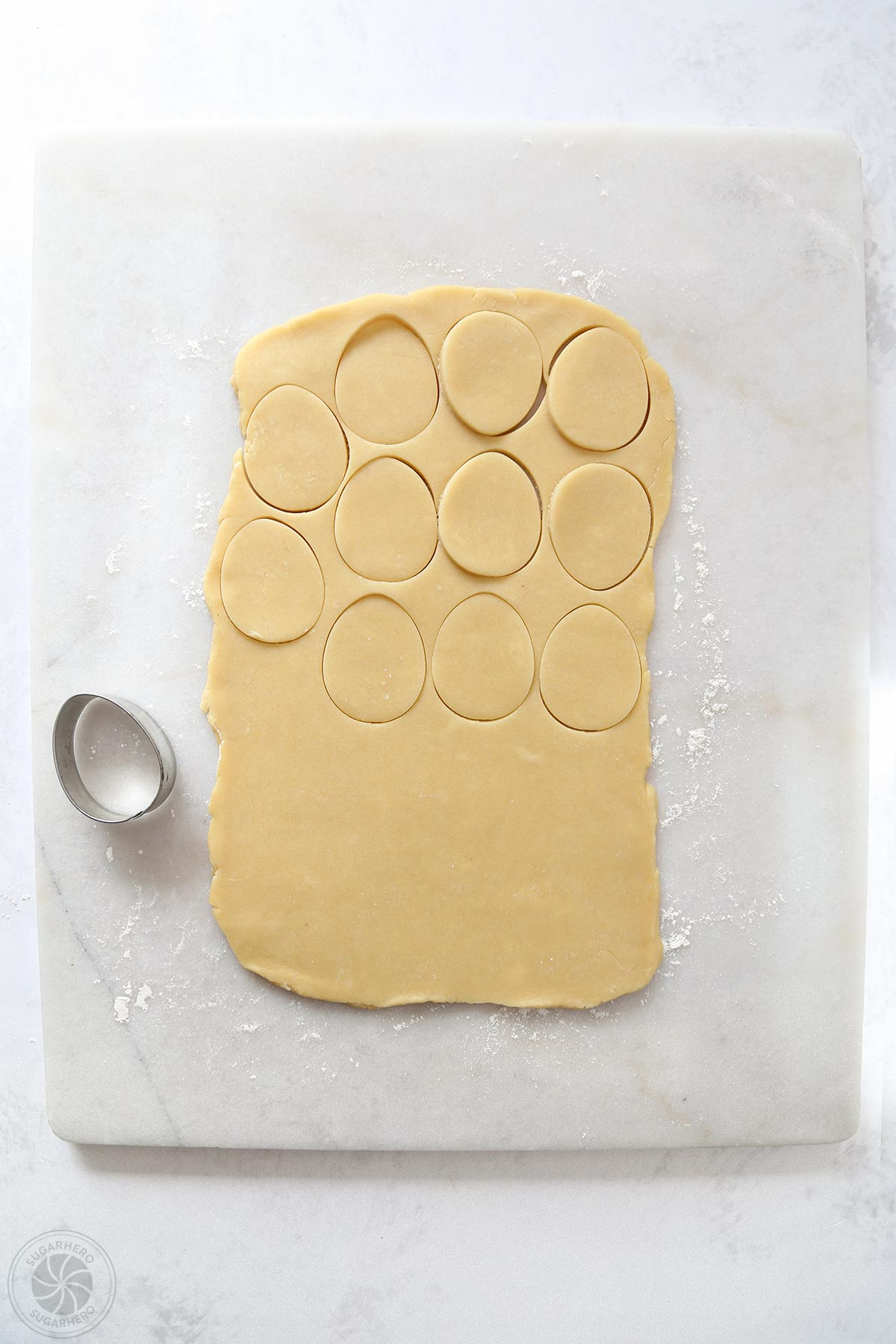 Sugar cookie dough rolled out on a marble slab, with egg shapes cut out of it.