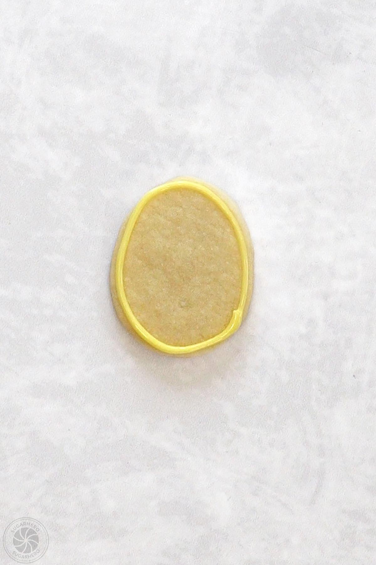 Egg-shaped sugar cookie with an outline of yellow royal icing around the edge.