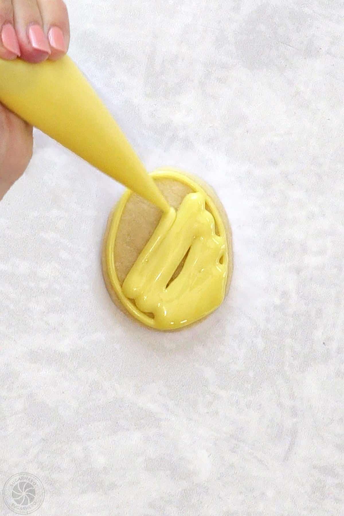 Egg-shaped sugar cookie being filled in with yellow royal icing.