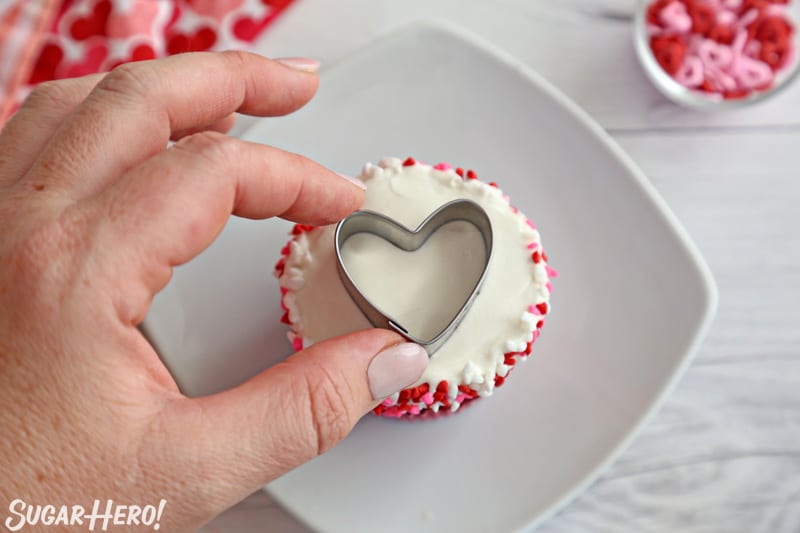 Placing a small heart-shaped cookie cutter on top of a cupcake