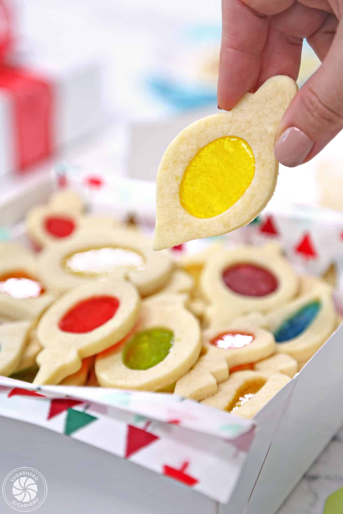 Hand holding a Stained Glass Cookie with a yellow center over a box of more cookies.