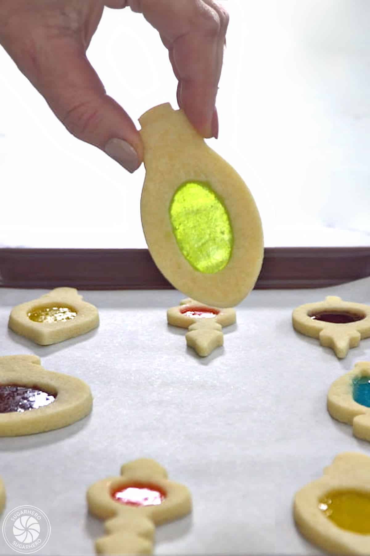 Hand holding up a fully cooled Stained Glass Cookie over a baking tray.