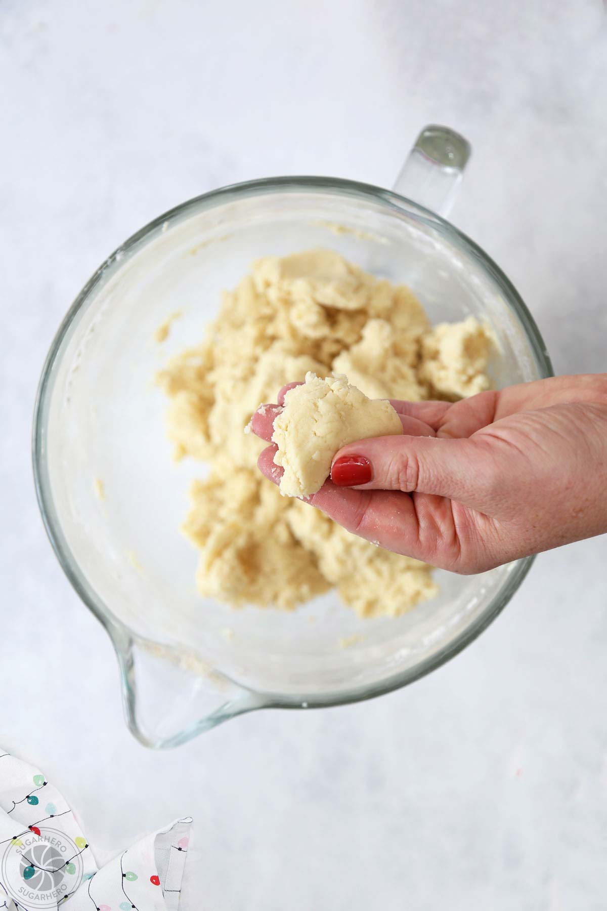 Hand holding a pinch of Stained Glass Cookie dough over a mixing bowl.