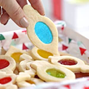 Hand holding a Stained Glass Cookie with a blue center over a box of more cookies.