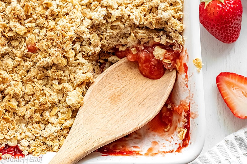 Wooden spoon scooping out Strawberry Crisp from the baking pan.