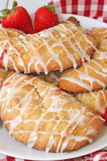 Strawberry Hand Pies stacked on a white plate by a checkered napkin and strawberries.