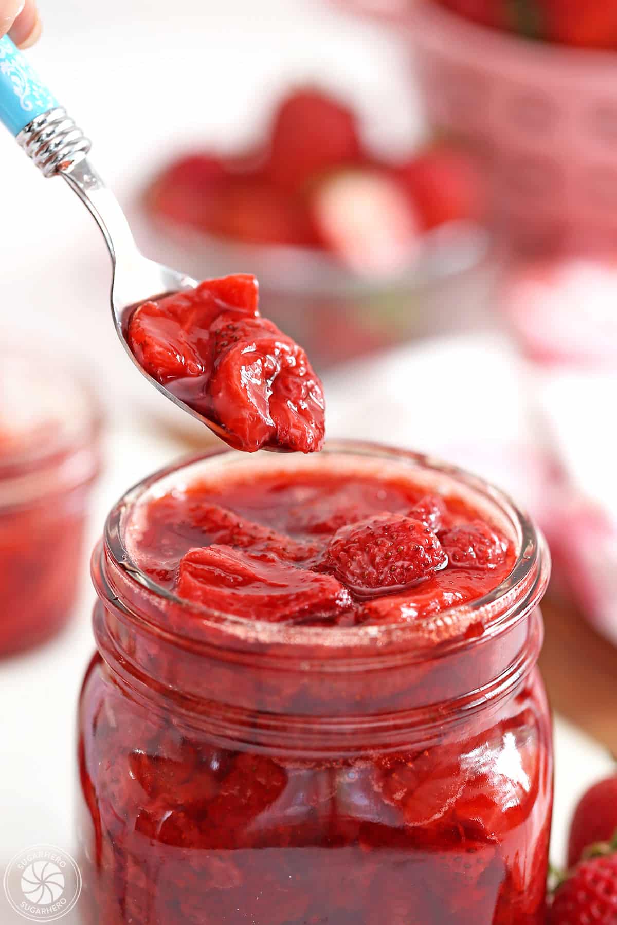Blue spoon scooping out a spoonful of Strawberry Sauce from a glass jar.