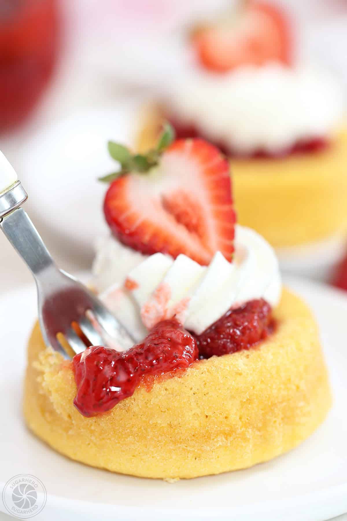 Fork taking a bite of angel food cake, strawberry sauce, and whipped cream.