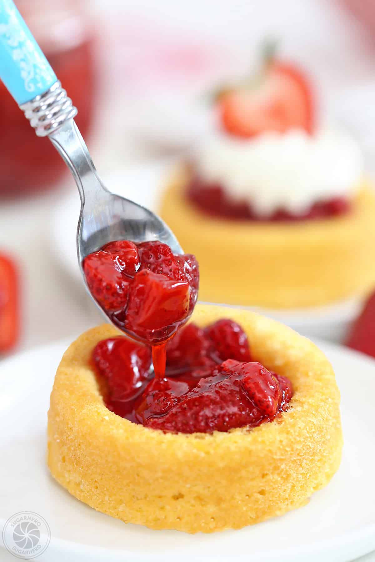 Blue spoon scooping Strawberry Sauce into an angel food cake cup.
