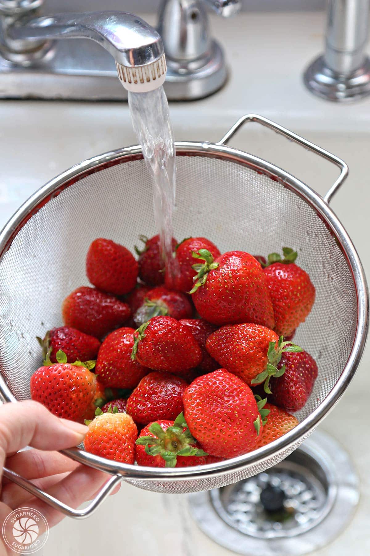 Rinsing fresh strawberries in a wire colander under running water.