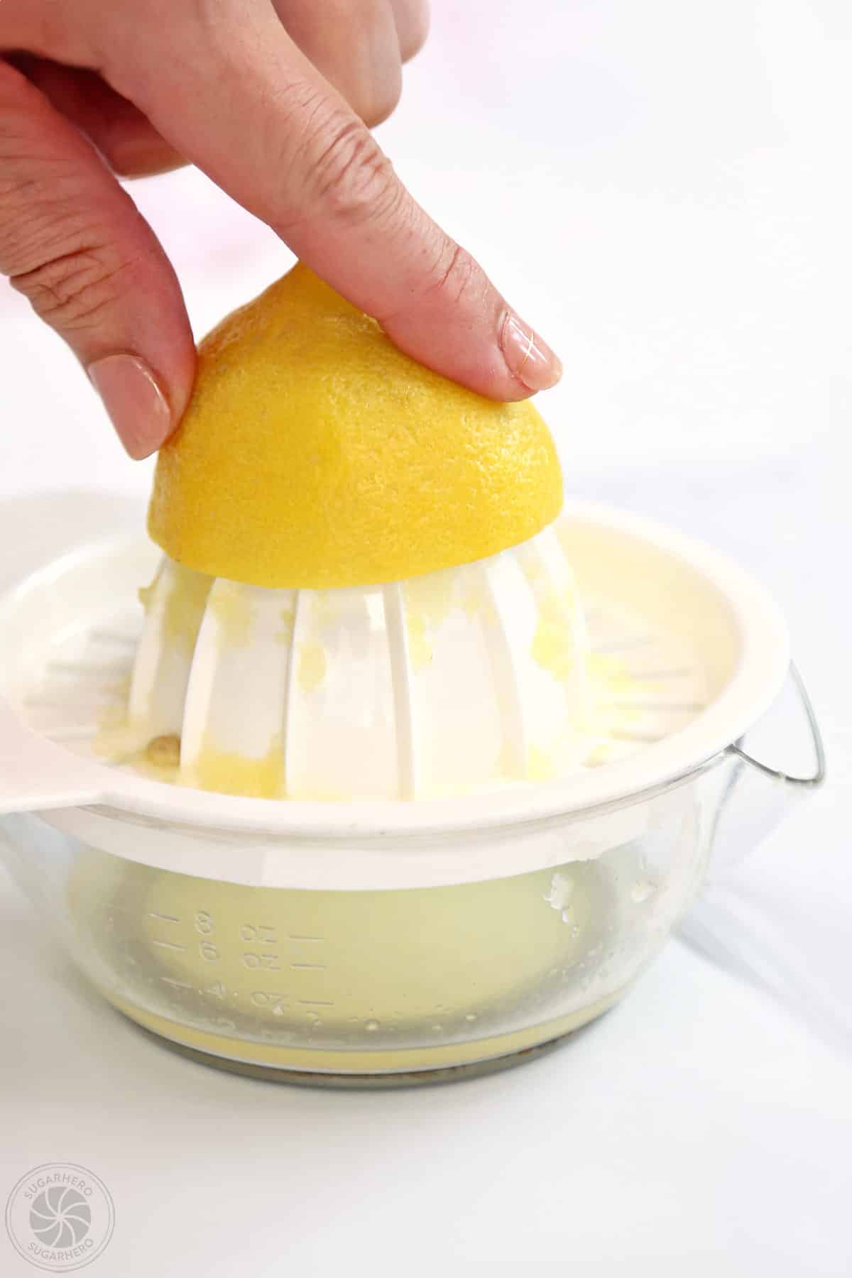 Juicing half of a lemon using a white hand juicer.