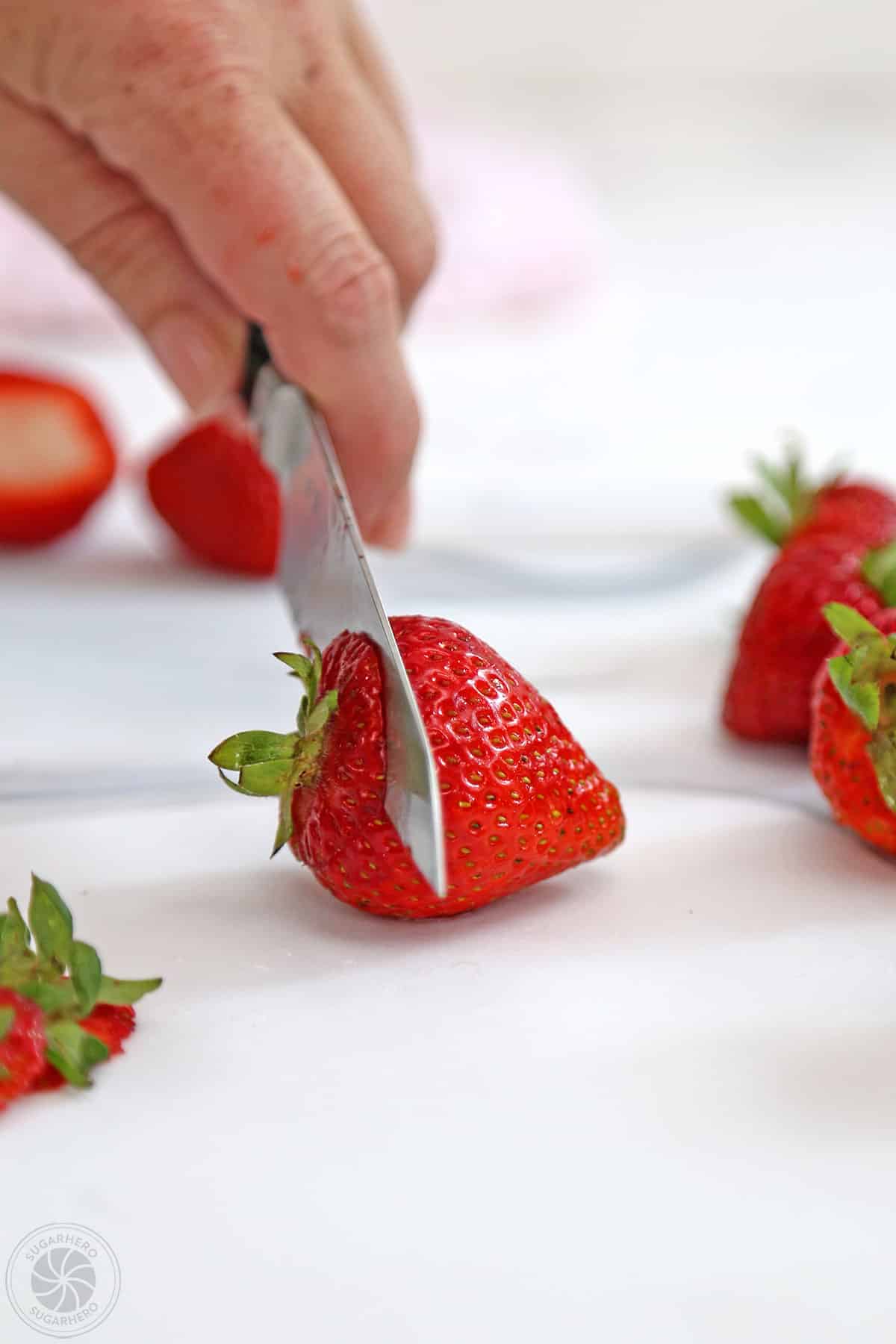 Hand using a knife to hull strawberry.