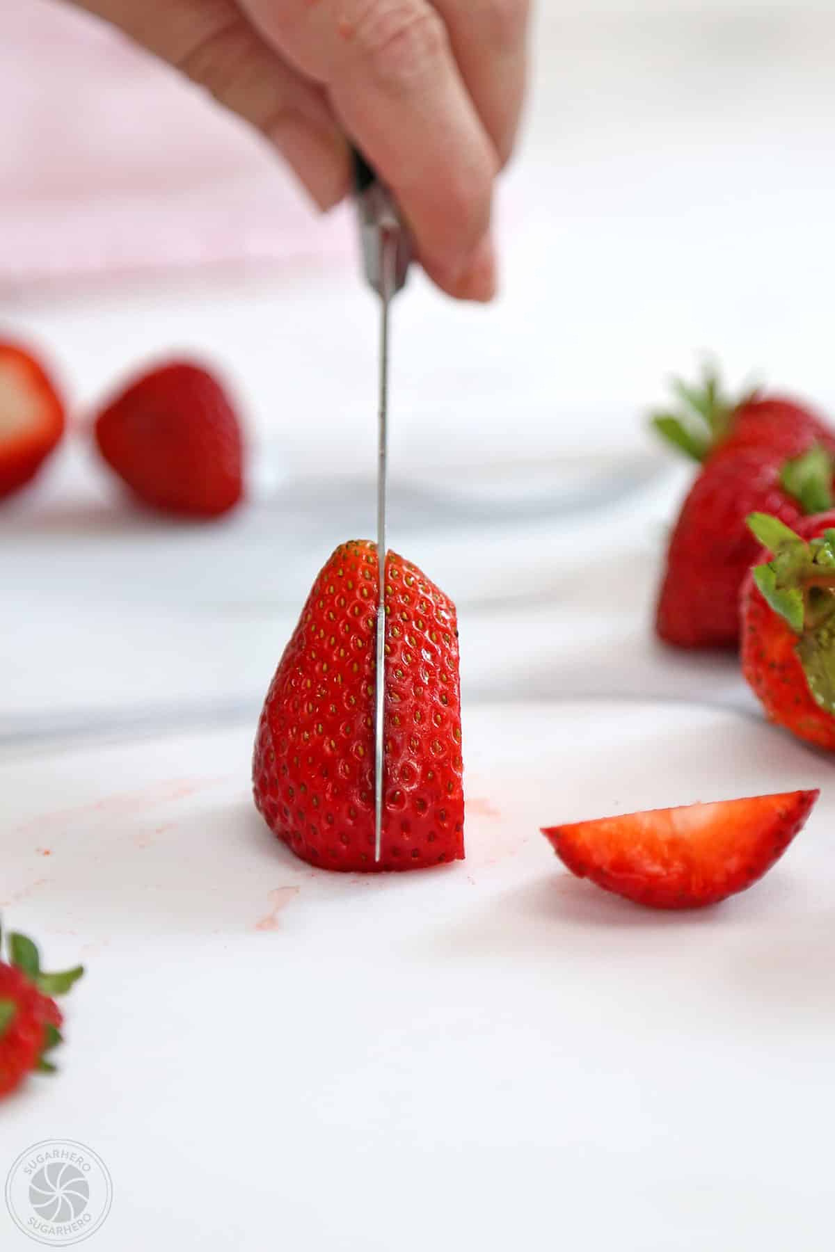 Hand using a knife to slice strawberry.