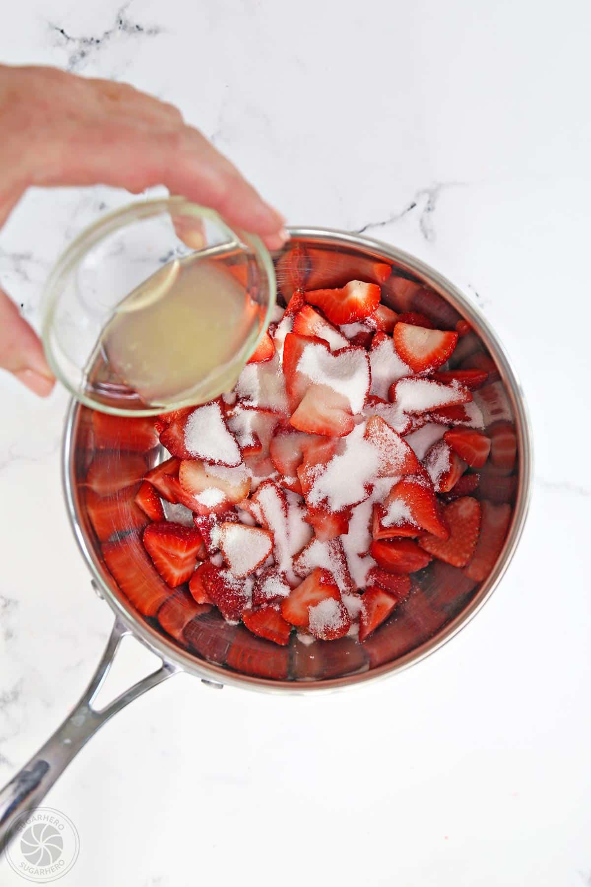 Pouring lemon juice into a saucepan with strawberries and sugar.