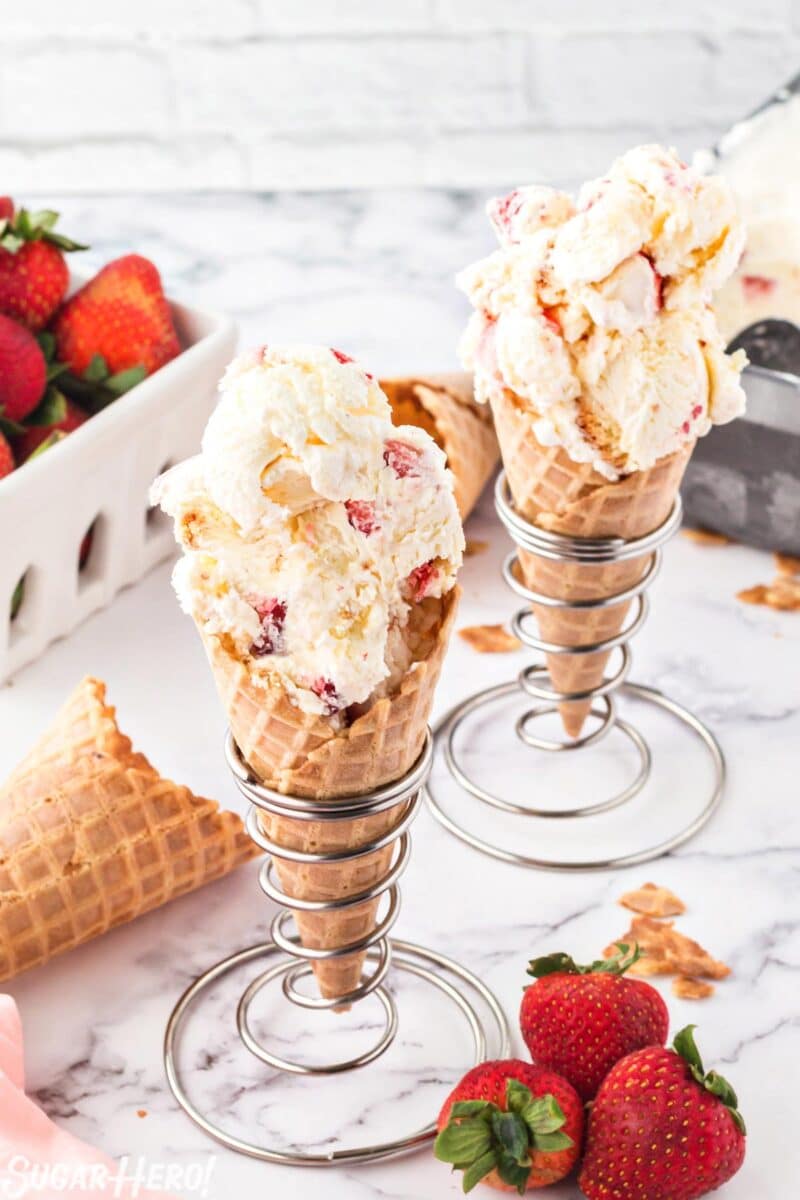 Top view of 2 waffle cones filled with scooped No-Churn Strawberry Shortcake Ice Cream with strawberries in the background.