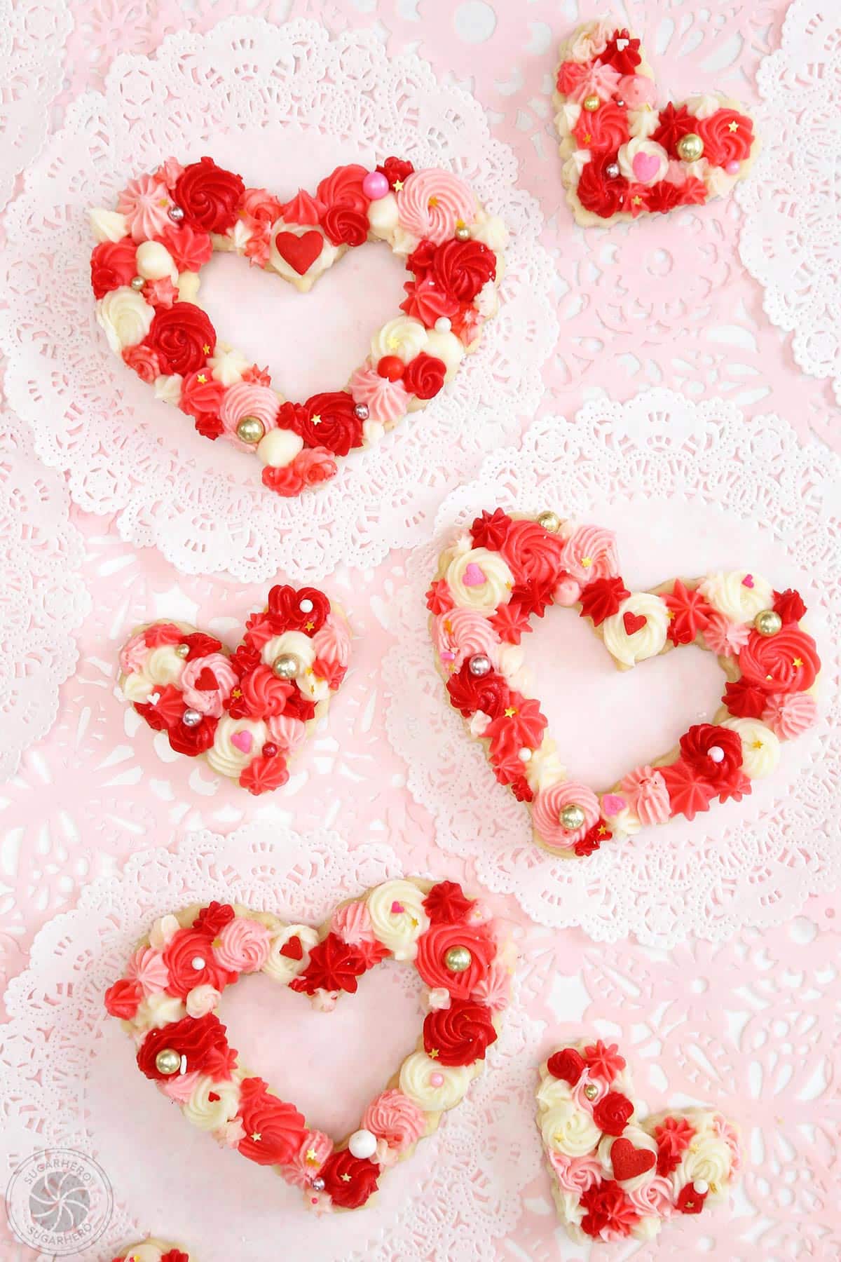 Overhead shot of 6 heart-shaped sugar cookies decorated with red, pink, and white frosting.
