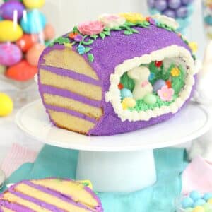 A Sugar Easter Egg Cake on a white cake platter with a slice cut off to show layers.