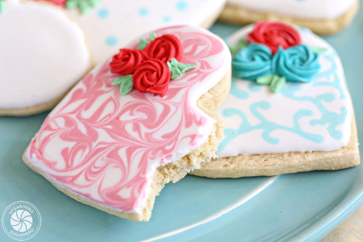 Close-up of two heart-shaped sugar cookies decorated with royal icing, with a bite taken out of one.