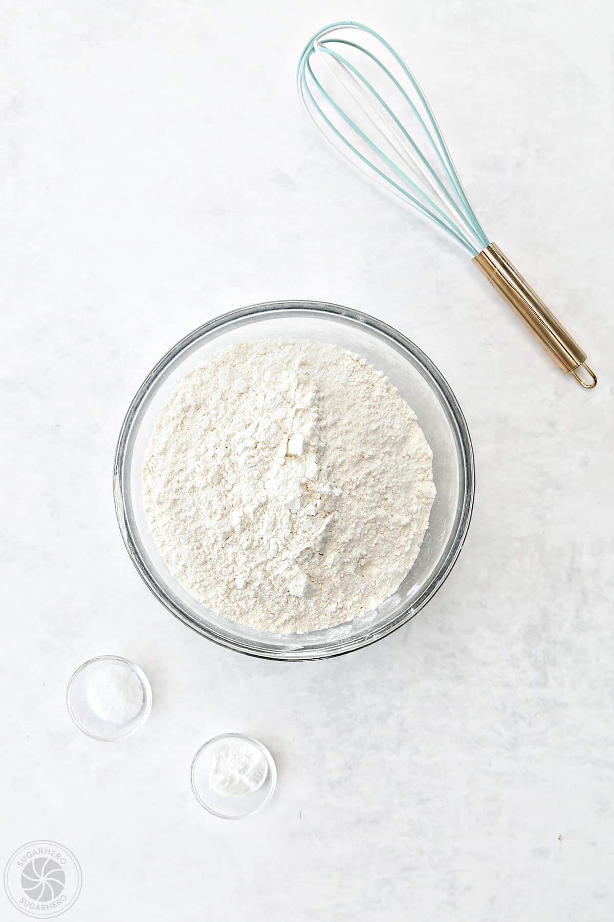 Bowls of flour, salt, and baking powder next to a whisk for sugar cookies.