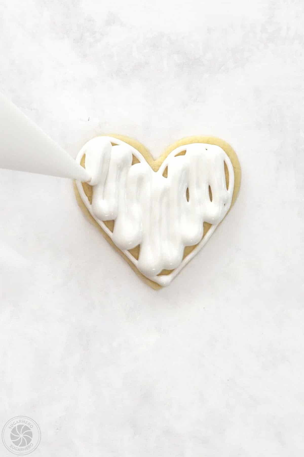 Piping bag flooding the center of a lined Valentine's Day Sugar Cookie with royal icing.