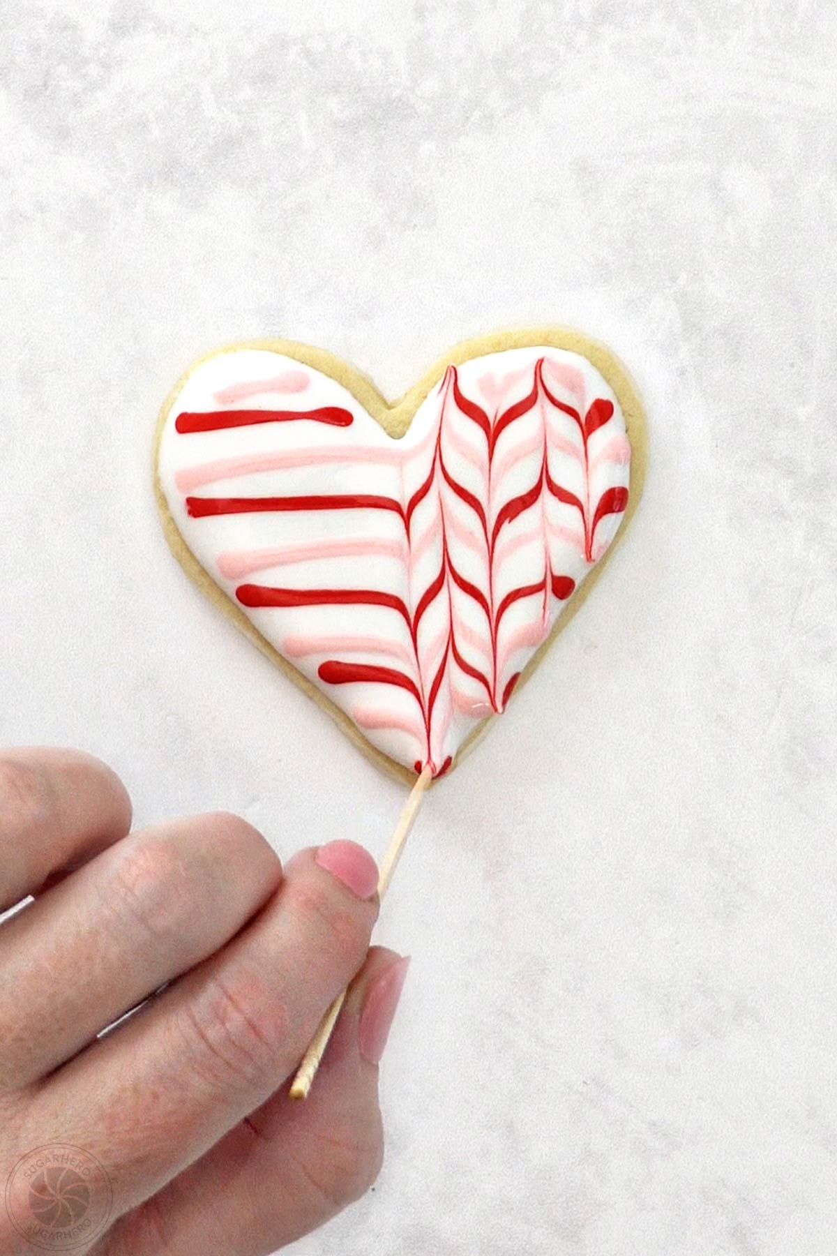Valentine's Day Sugar Cookie with a hand running a toothpick through the red and pink lines to make a zig-zag pattern.