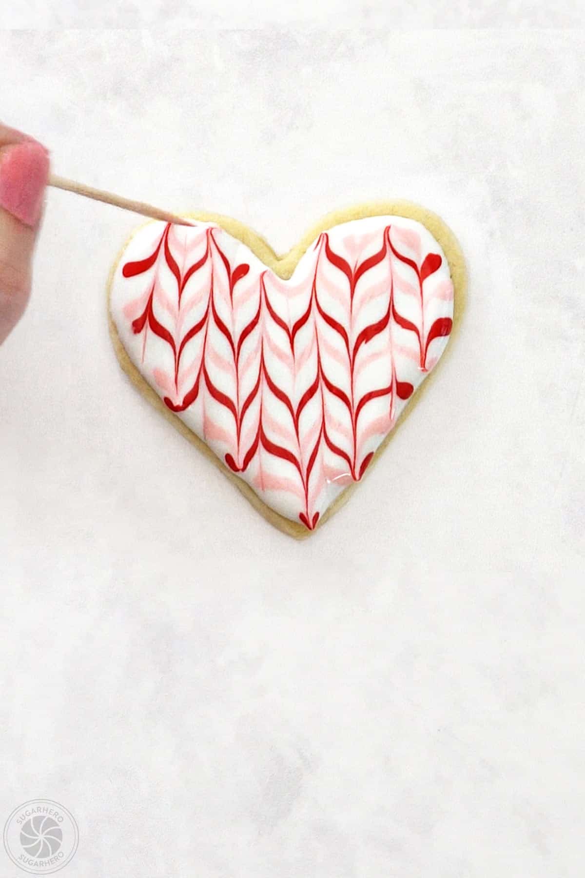 Valentine's Day Sugar Cookie with a hand using a toothpick to finish a zig-zag pattern.