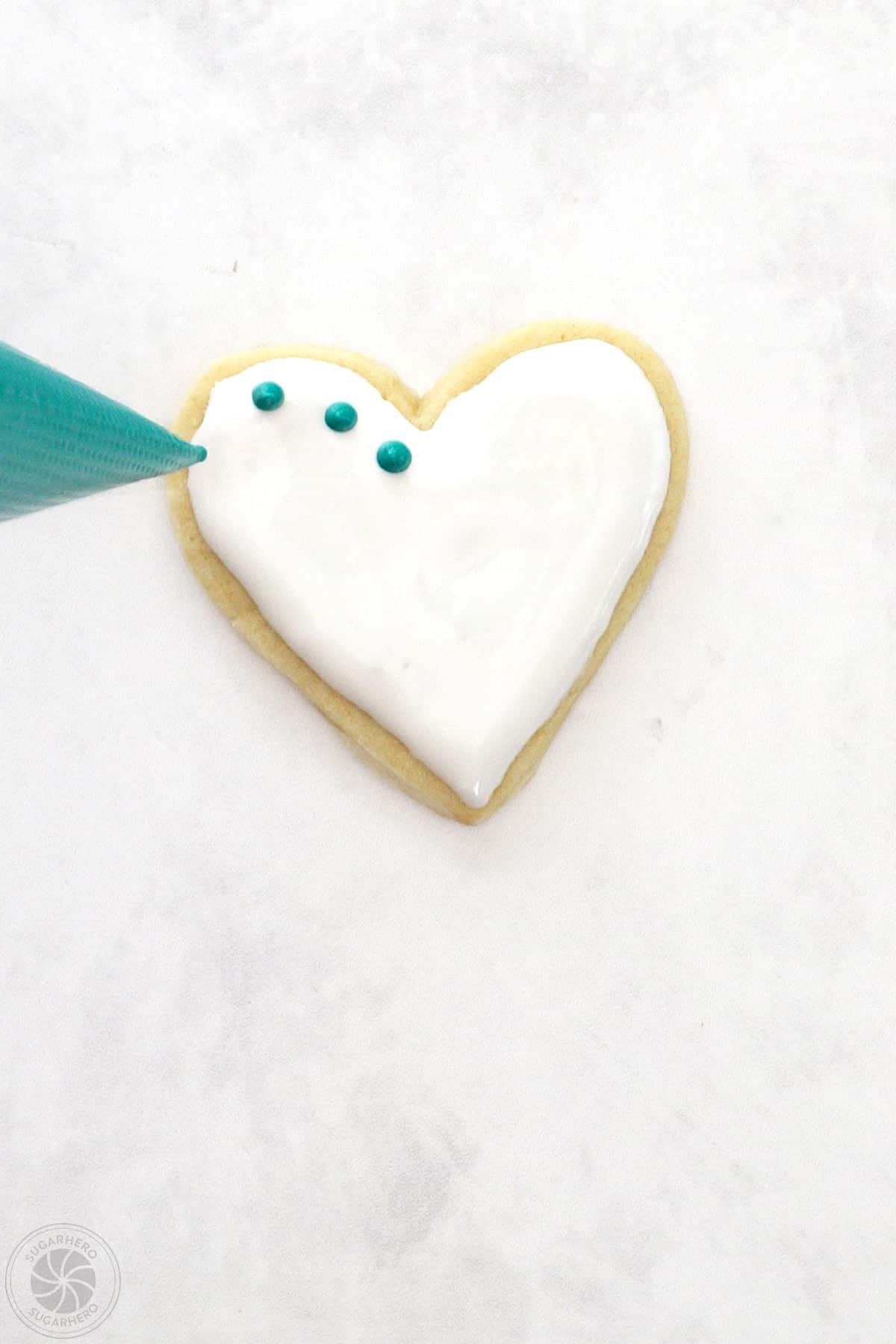 Hand piping small dots around the outside of a Valentine's Day Sugar Cookie.