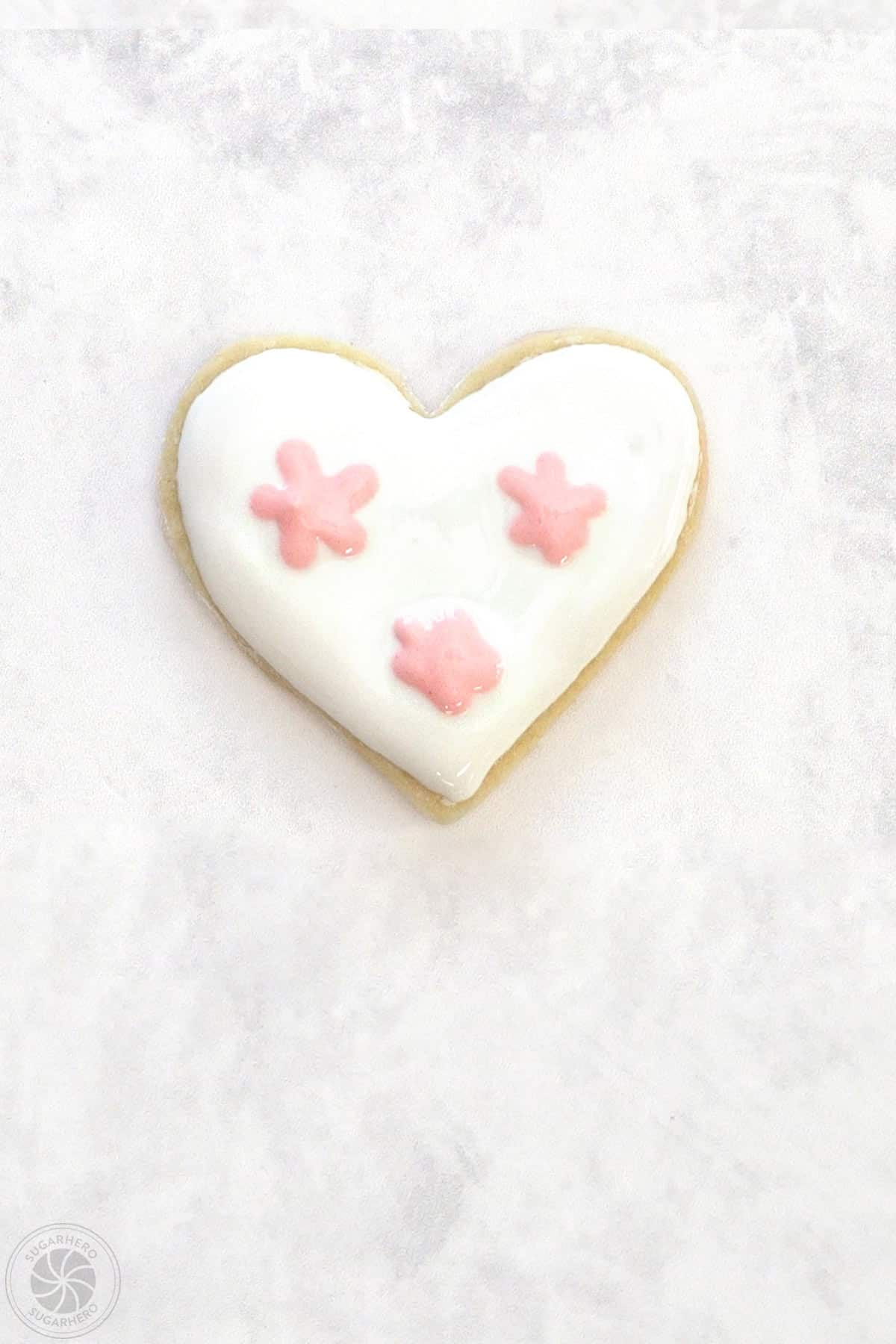 A Valentine's Day Sugar Cookie with 3 light pink clusters of royal icing.