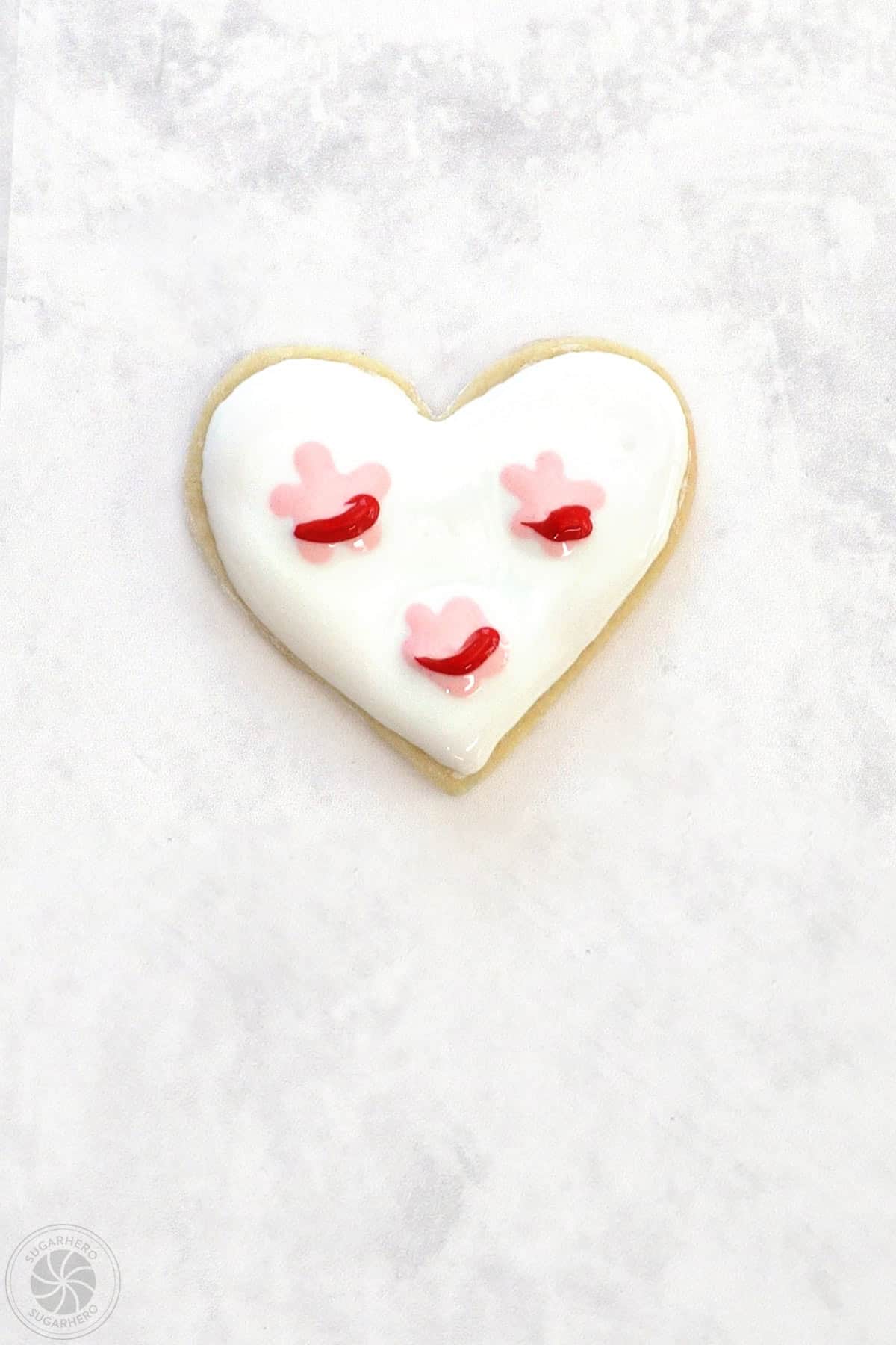 A Valentine's Day Sugar Cookie with 3 light pink clusters of royal icing with a red stripe across them.