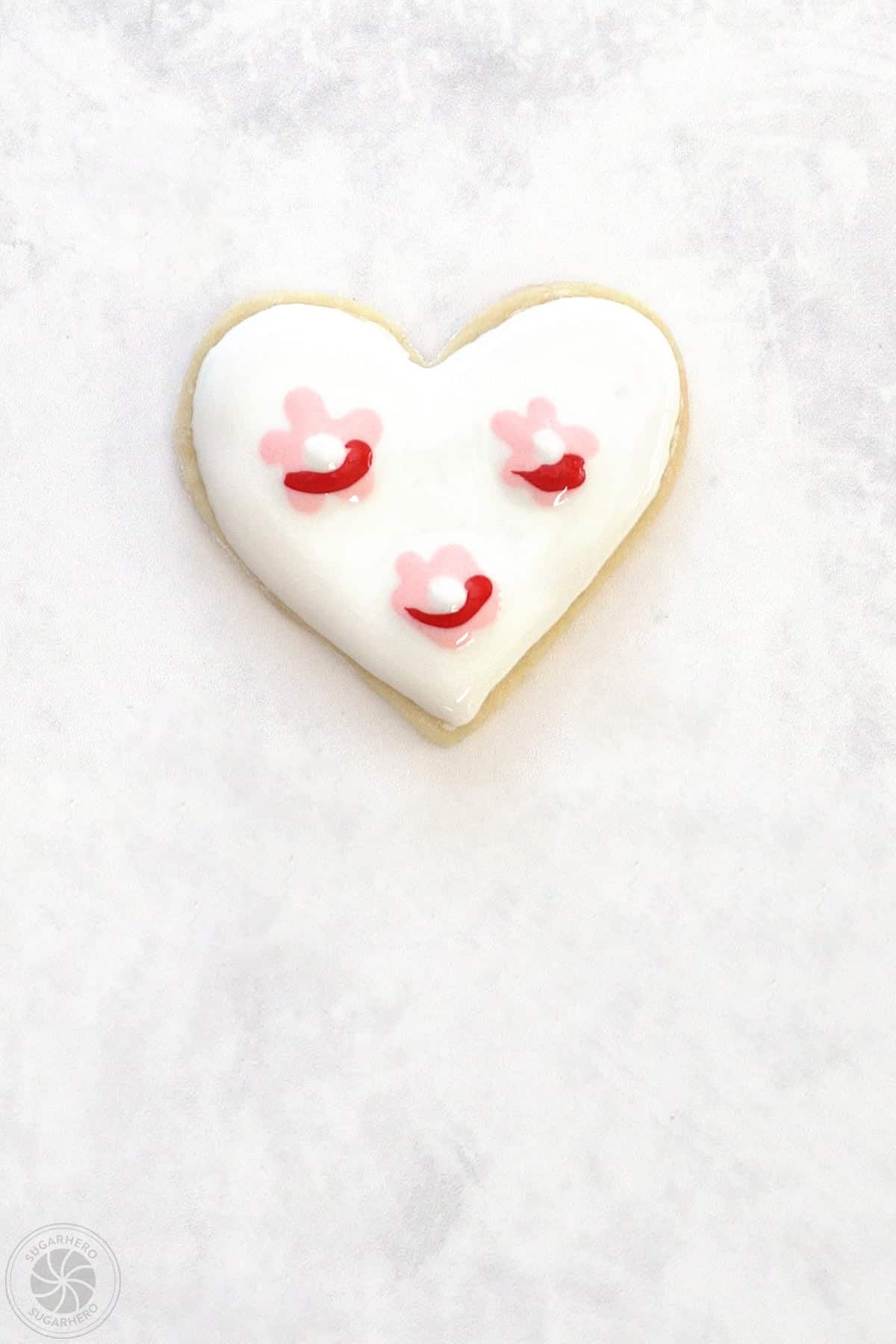 A Valentine's Day Sugar Cookie with 3 light pink clusters with a red line and white dot of royal icing on them.