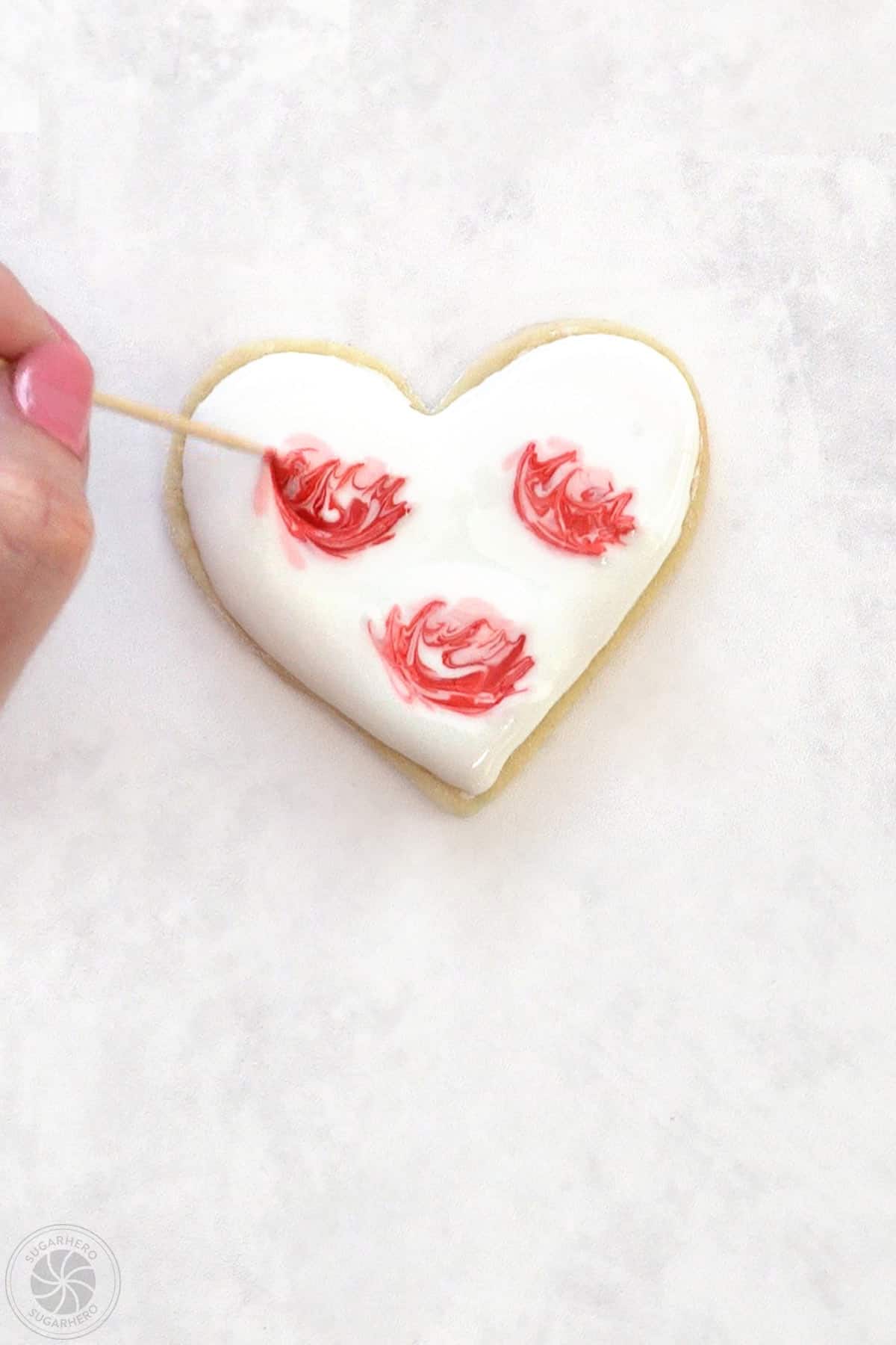 Hand using a toothpick to swirl the clusters of royal icing to make them look like abstract roses.