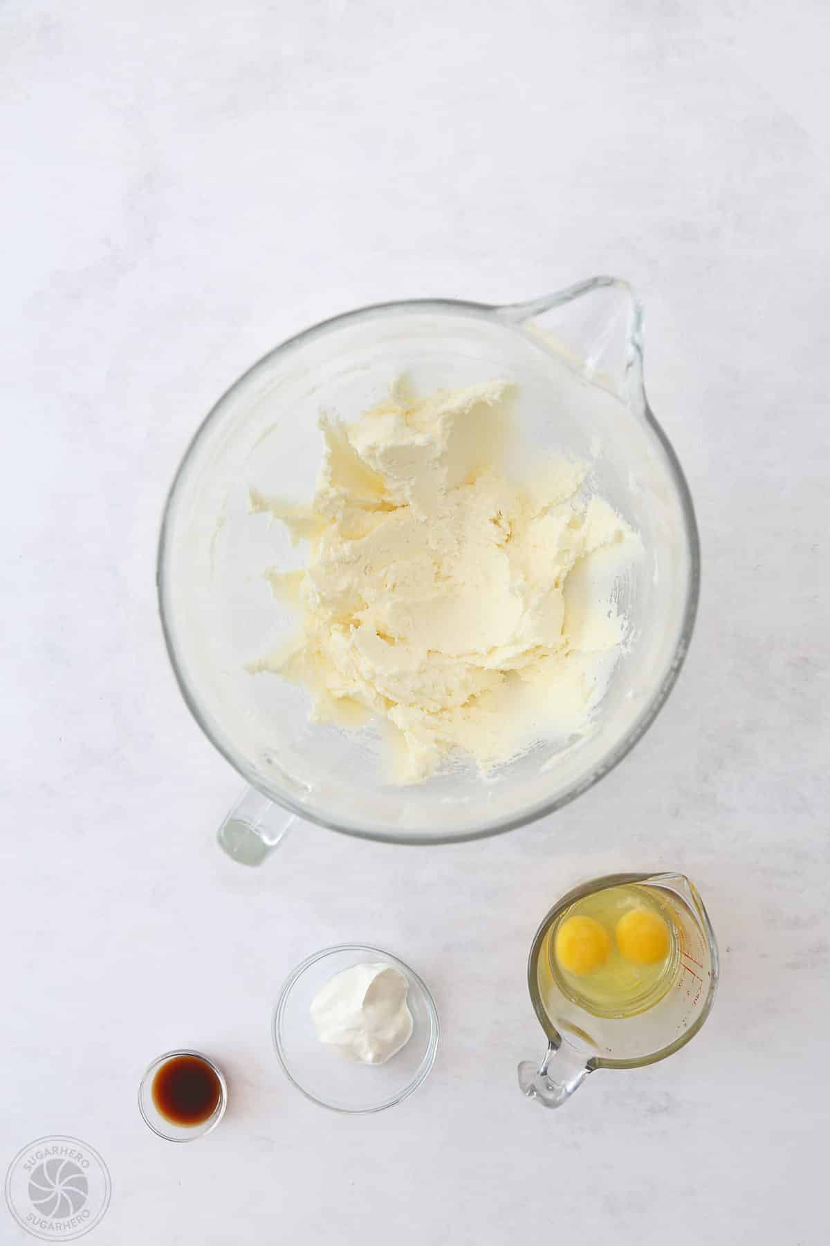 Creamed butter and sugar in a bowl next to smaller containers of vanilla, sour cream and eggs for sugar cookies.