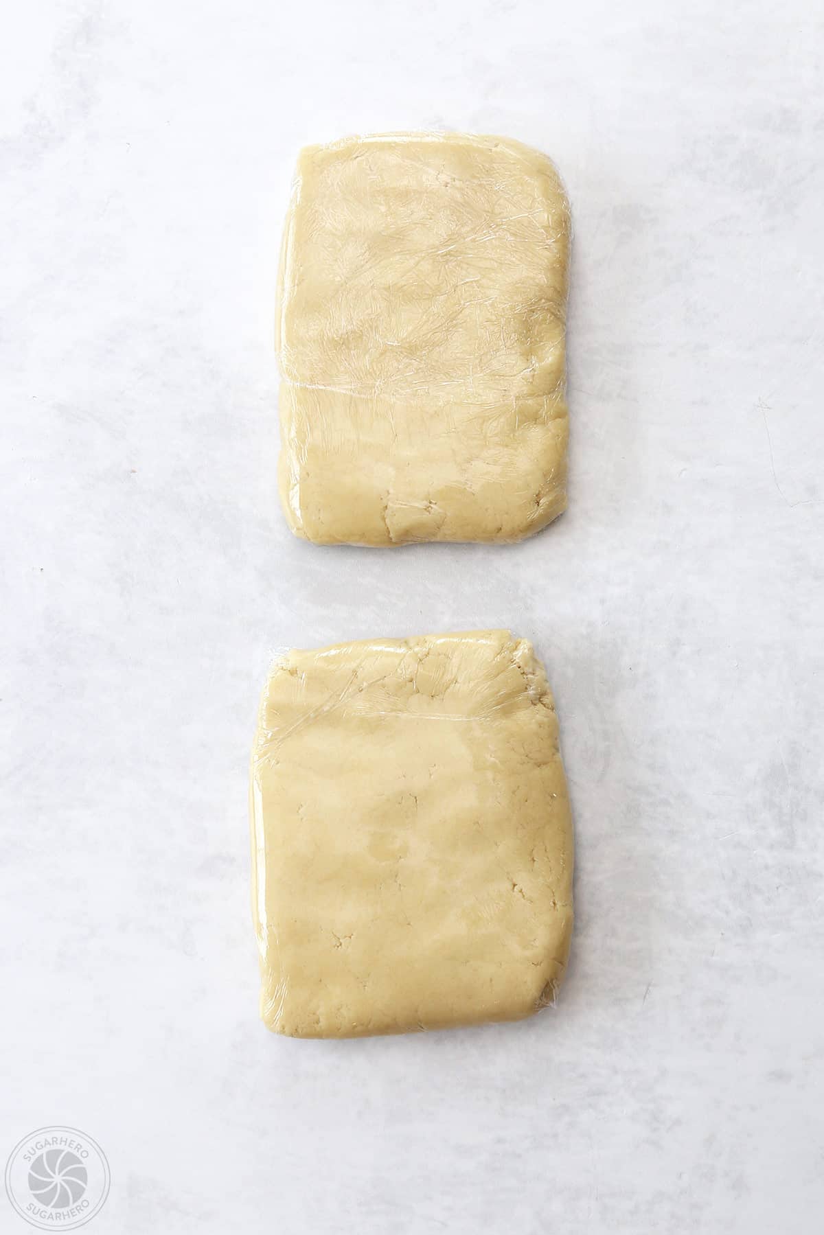 Two discs of sugar cookie dough wrapped in plastic wrap.