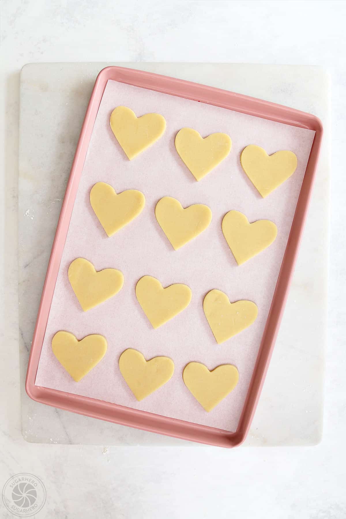 A parchment paper lined baking sheet covered in unbaked heart shaped sugar cookies.
