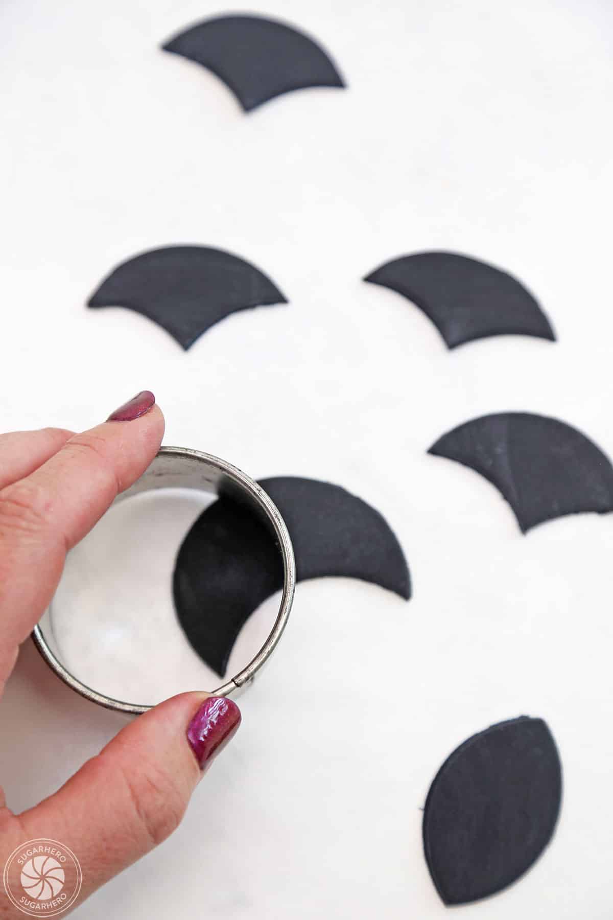Hand pressing a circular cutter onto black fondant to make the top of the vampire head.