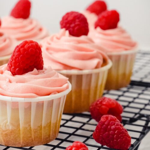 Vanilla Raspberry Cupcakes sitting on a black cooling rack next to fresh raspberries.