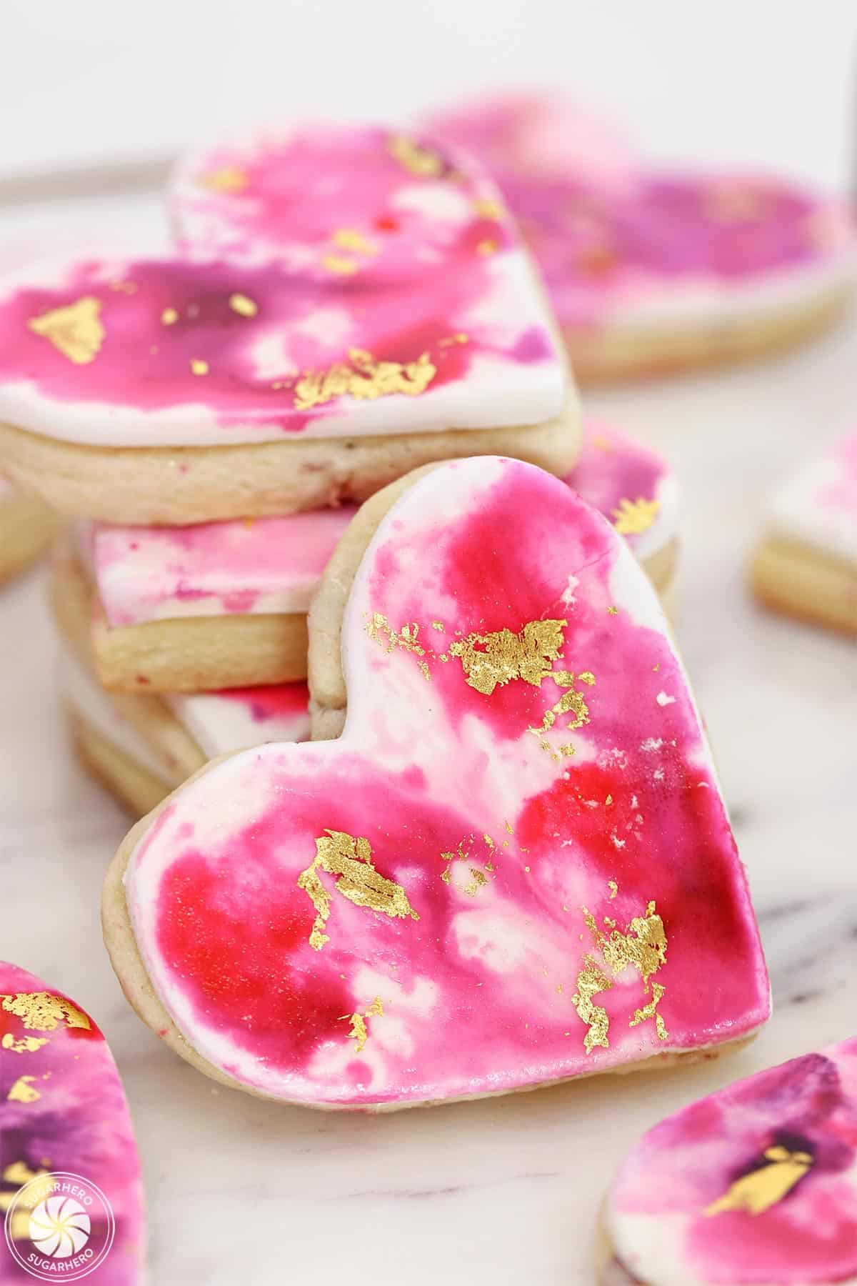 A Watercolor Rose Sugar Cookie propped up next to a stack of more cookies.